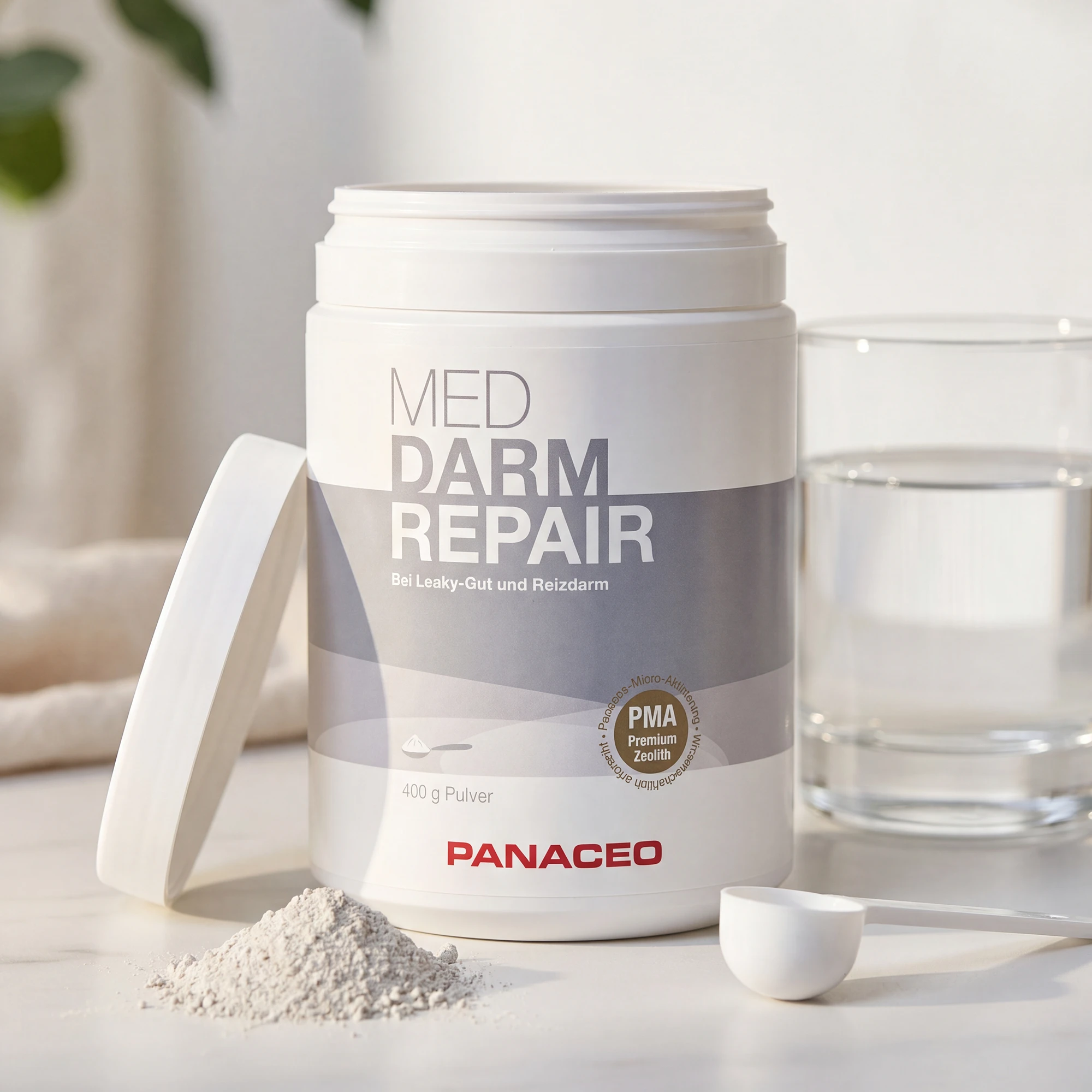 Geöffnete Dose PANACEO MED DARM REPAIR Pulver 400 g mit Messlöffel, Pulverhaufen und Wasserglas auf hellem Untergrund
