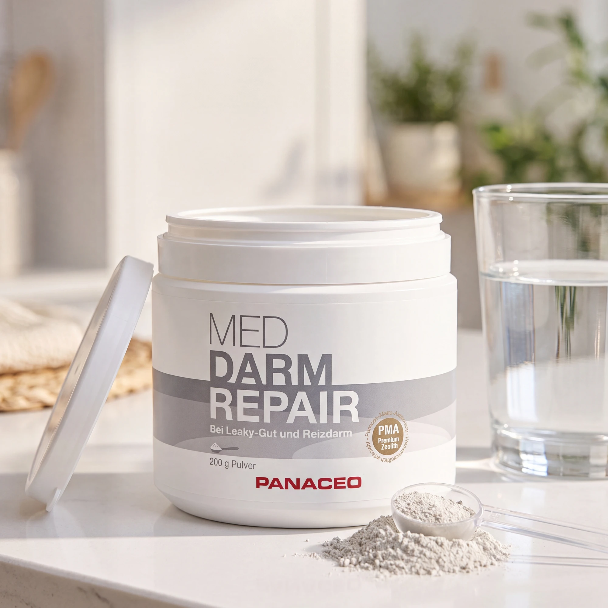 PANACEO MED DARM REPAIR Pulver 200 g Dose mit Messlöffel und Glas Wasser PANACEO MED DARM REPAIR Pulver 200 g in geöffneter Dose mit Messlöffel voller Pulver und Glas Wasser auf heller Küchenfläche