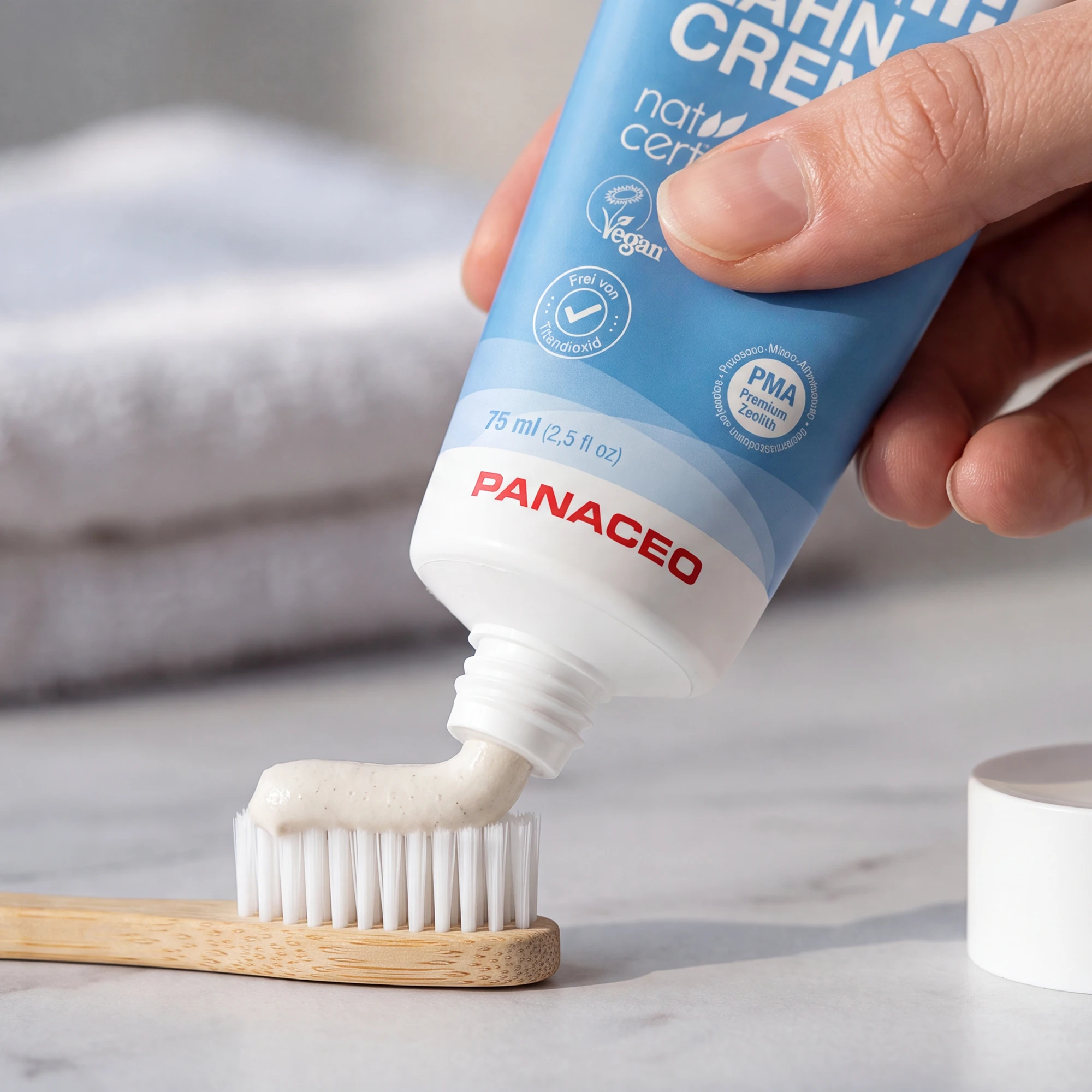 PANACEO Care Zeolite Toothpaste 75 ml on toothbrush – natural periodontal toothpaste with PMA zeolite Hand applying PANACEO Care Zeolite Toothpaste 75 ml onto a bamboo toothbrush; fluoride-free, vegan toothpaste with PMA zeolite, organic mint oil and aloe vera, without titanium dioxide.