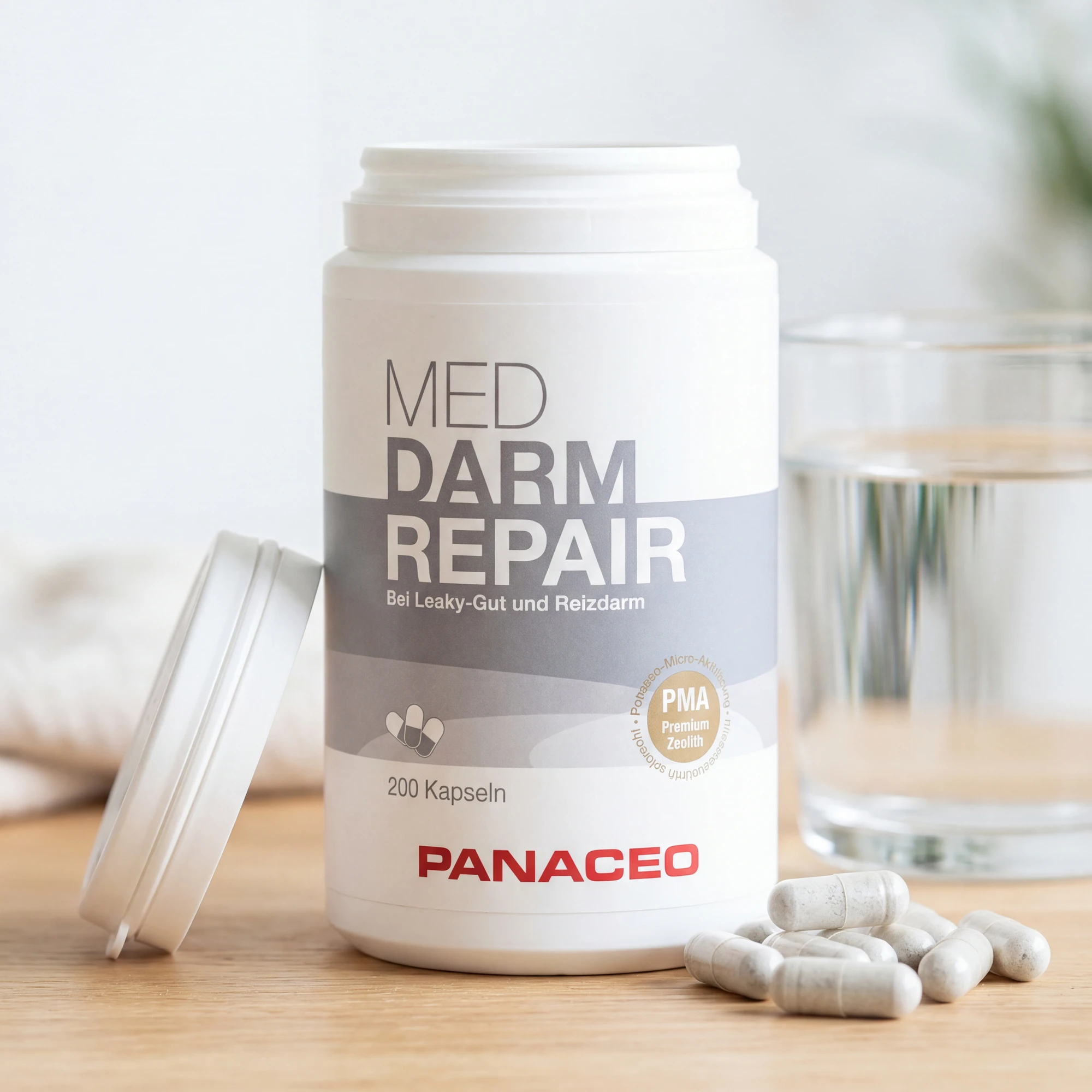 PANACEO MED DARM REPAIR Kapseln 200 Stk. – Produktdose mit geöffnetem Deckel und Kapseln PANACEO MED DARM REPAIR Kapseln 200 Stk. in weißer Dose, geöffnet mit Kapseln auf Holzfläche neben einem Glas Wasser