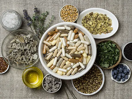 Eine Auswahl an Nahrungsergänzungskapseln in einer Schale, umgeben von frischen Kräutern, Samen und natürlichen Zutaten. Symbol für natürliche Vitamine und Mineralstoffe mit PANACEO Green Health.