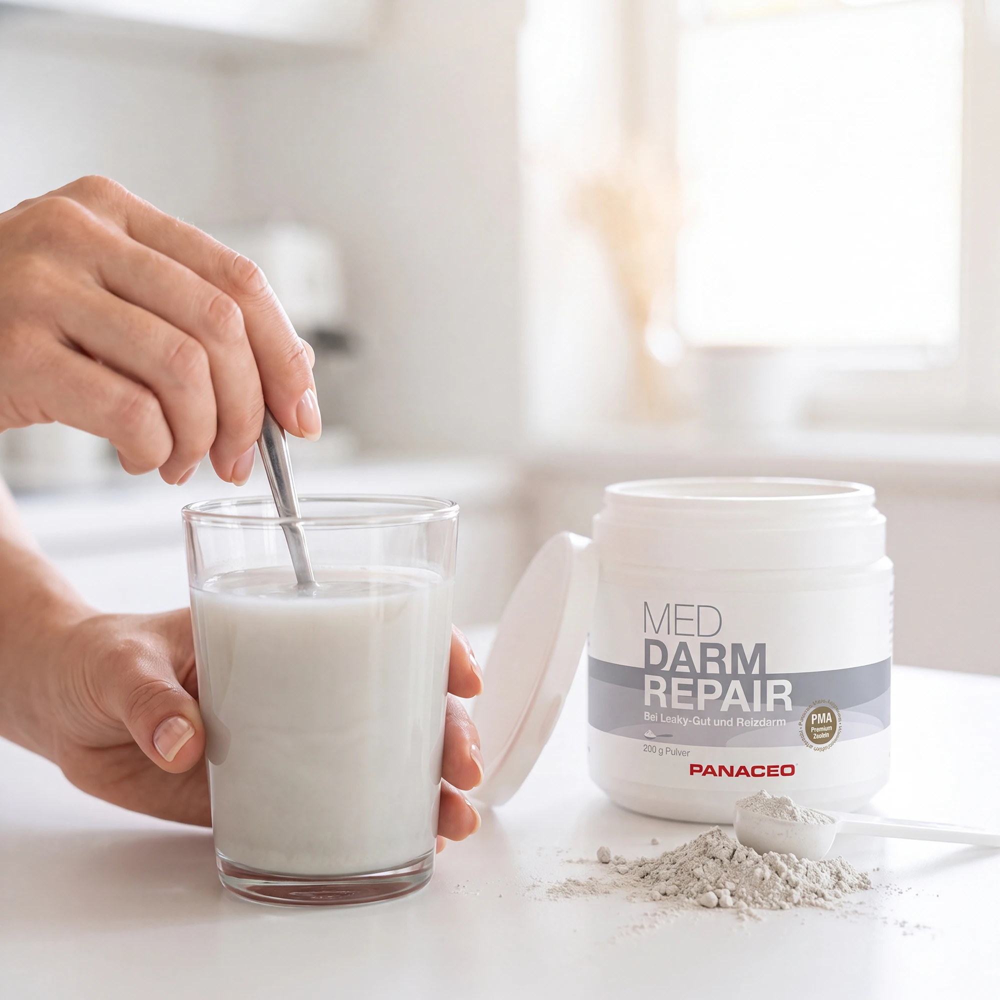 Hand rührt PANACEO MED DARM REPAIR Pulver 200 g in ein Glas Wasser, daneben geöffnete Dose und Messlöffel mit Pulver.