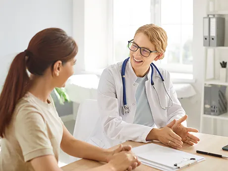 Eine Ärztin spricht freundlich mit einer Patientin am Schreibtisch. Das Bild symbolisiert Vertrauen, medizinische Beratung und Unterstützung bei Darmtherapie mit PMA-Zeolith.